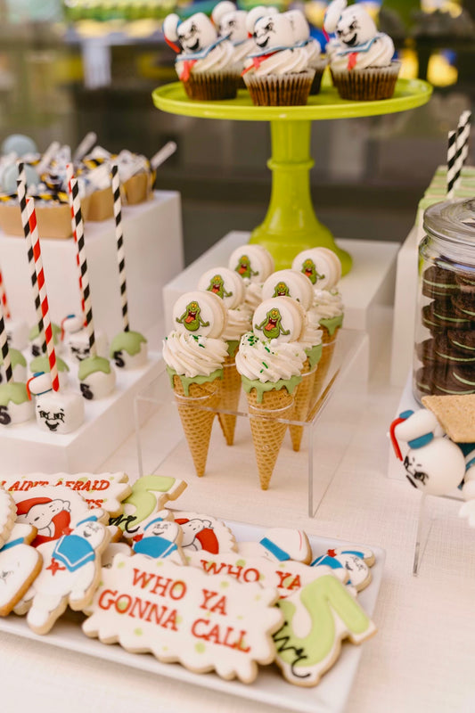 Decorative cookies and ice cream cones on a table with a green stand in the background.