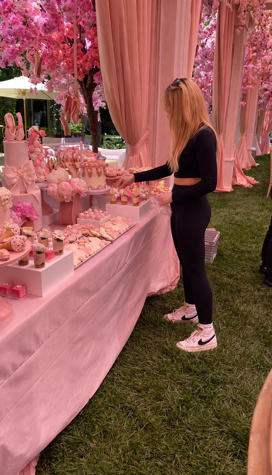 Woman standing next to a pink dessert table with cherry blossom trees in the background