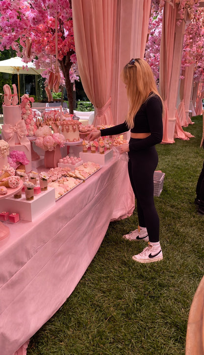 Woman standing next to a pink dessert table with cherry blossom trees in the background