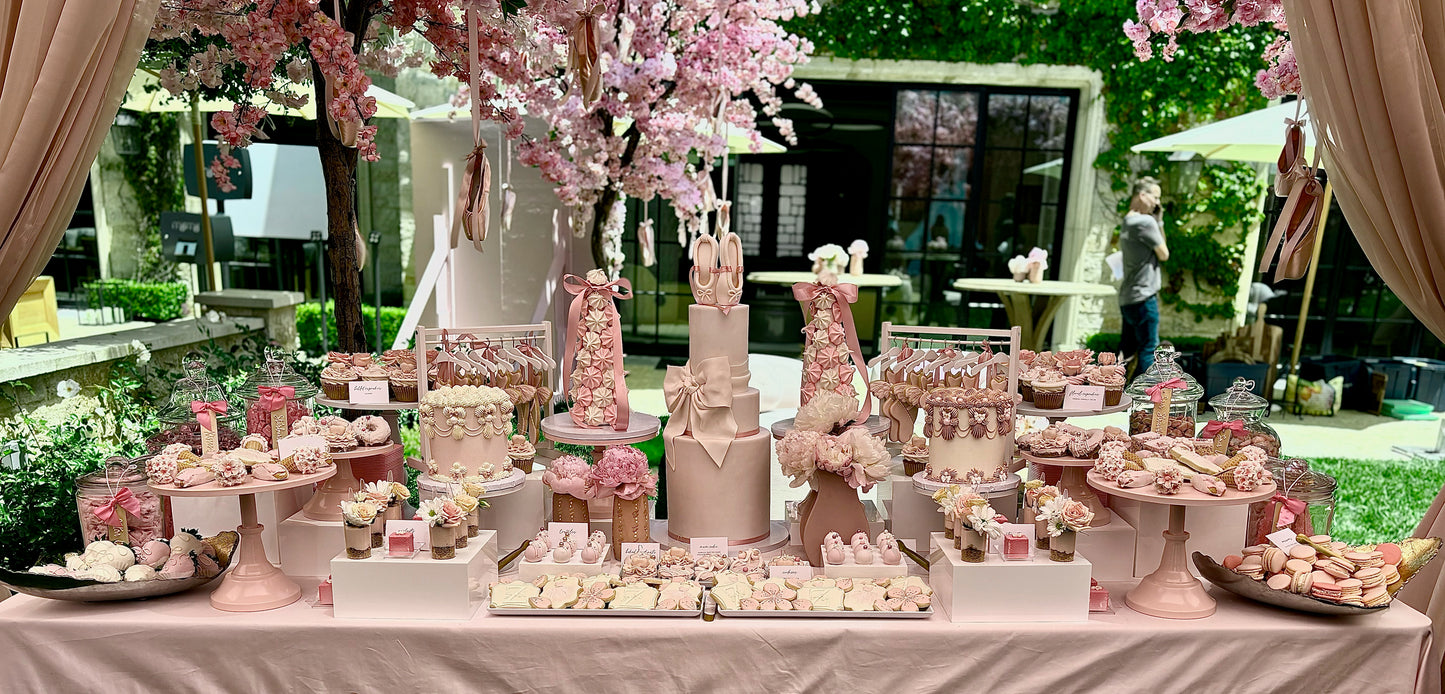 Decorative table with pink-themed desserts and flowers in an outdoor setting