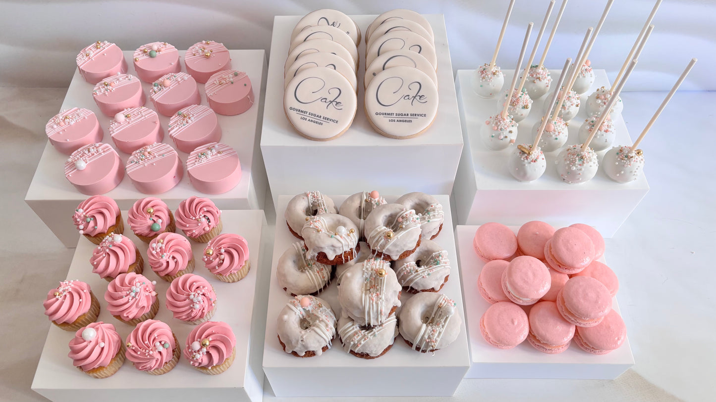 Assorted desserts including cookies, cupcakes, and macarons on a white surface.
