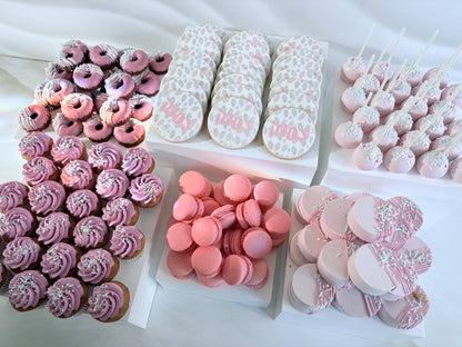 Assorted pink-themed pastries including donuts, cookies, and macarons on a white surface.